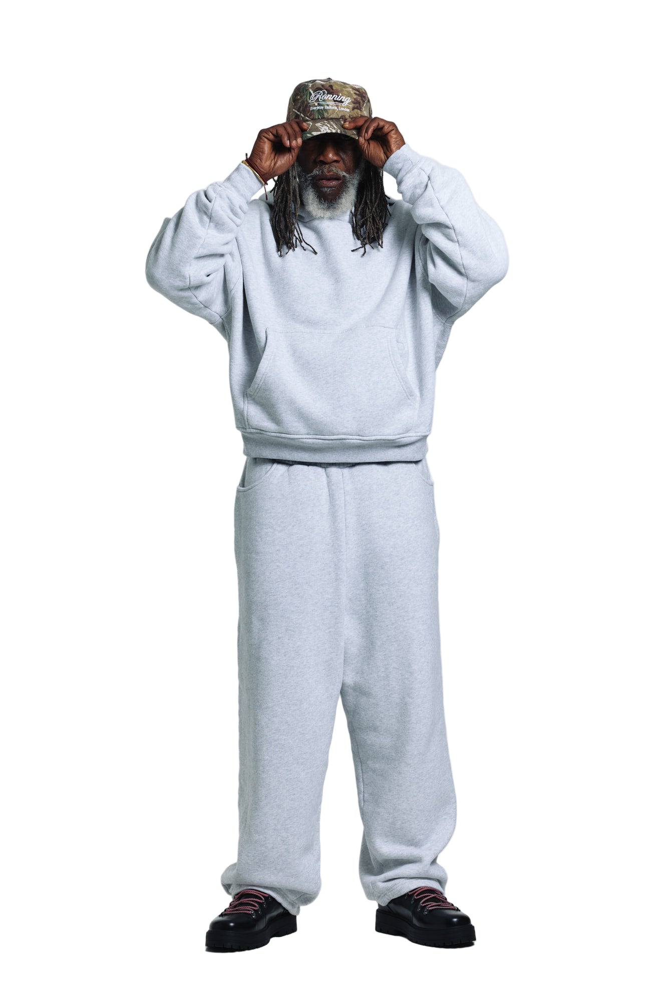 Person wearing a gray sweatshirt and pants with a cap on a white background