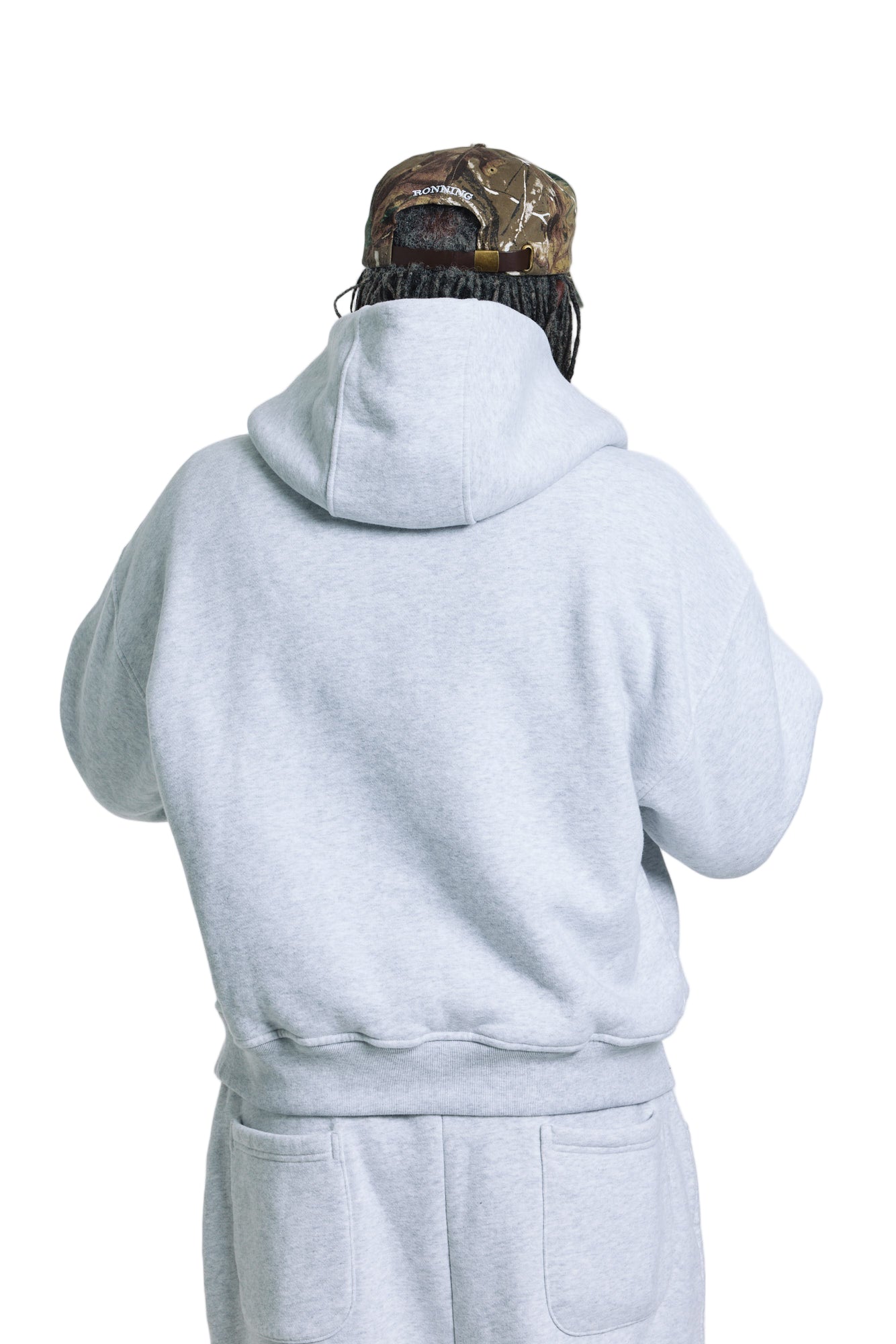 Person wearing a gray hoodie and camouflage cap on a white background